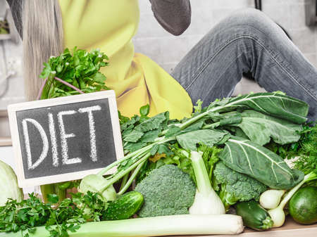 Young woman in kitchen having many green vegetables presenting board with diet sign.のeditorial素材