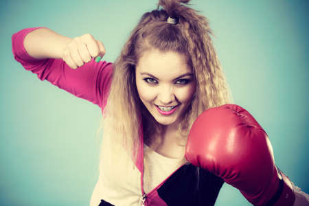 Funny blonde girl female boxer in big fun red gloves playing sports boxing studio shot on blue