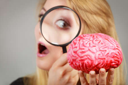 Blonde woman holding magnifying glass investigating something and looking closely at fake brain.のeditorial素材