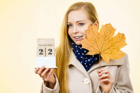 Woman holding calendar with first autumn day 22 september and big leaf. Studio shot on yellow background.のeditorial素材
