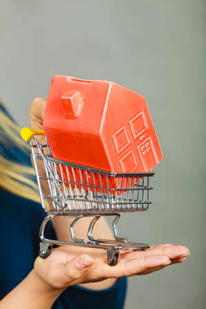 Buying property or home, real estate investment concept. Woman hand holding shopping cart with house insideの写真素材