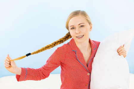 Bedding fabric softener concept. Young woman wearing cute pink pajamas hugging soft pillowの写真素材