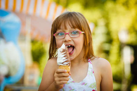 Summertime joy, summer recreation outside concept. Toddler girl in eyeglasses eating ice cream, having funの写真素材