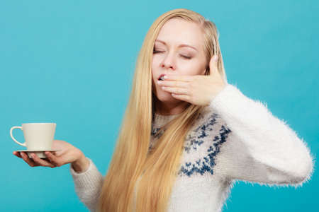 Addiction and caffeine need concept. Sleepy yawning blonde woman holding cup of coffee about to drink it.の写真素材