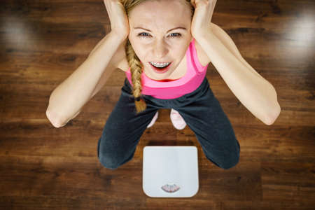 Scared teenage woman on bathroom scale machine thinking about weight loss and proper body mass. Being fit and healthy concept.の写真素材