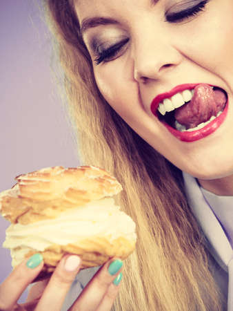 Sweet food and happiness concept. Funny joyful blonde woman holding yummy choux puff cake with whipped cream, excited crazy face expression. On violetの写真素材