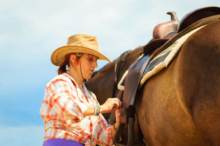 Taking care of animals, horsemanship, equine concept. Cowgirl getting horse ready for ride on countryside.の写真素材