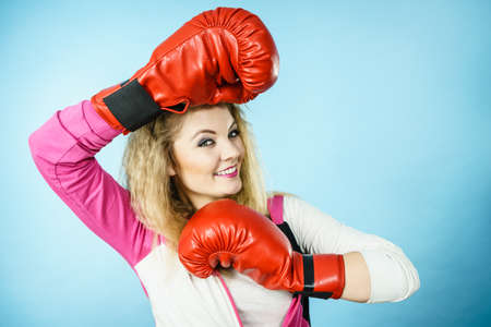 Funny blonde girl female boxer in big fun red gloves playing sports boxing studio shot on blue