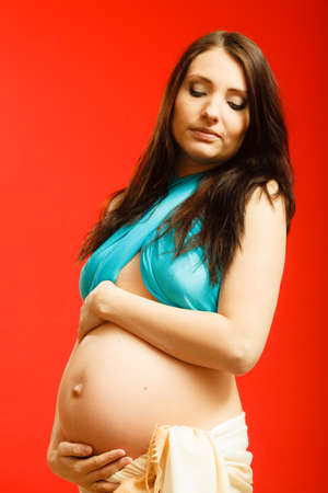 Parenthood, waiting for baby concept. Adult woman showing her big pregnant belly. Indoor shot on red backgroundの写真素材