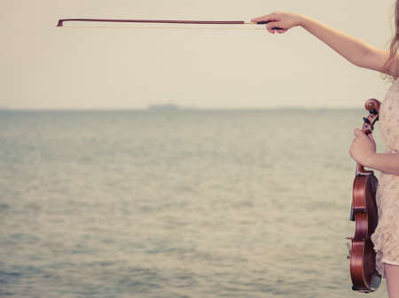 Music love, hobby and everyday passion concept. Woman on beach near sea holding violinの写真素材