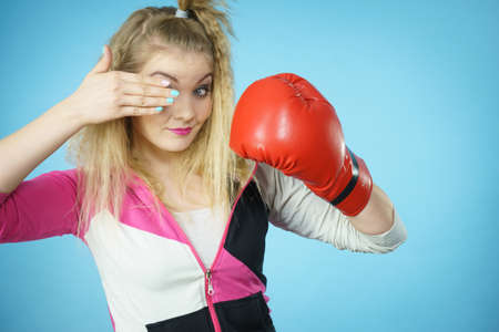 Funny blonde girl female boxer in big fun red gloves playing sports boxing studio shot on blueの写真素材