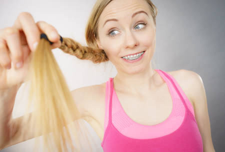 Happy woman looking at her long blonde hair ends, seeing positive effects of using conditioner....
