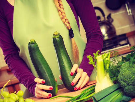 Woman in kitchen holding green fresh zucchini vegetable. Young housewife cooking. Healthy eating, vegetarian food, dieting and people concept.のeditorial素材