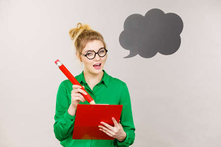 Young business woman wearing jacket intensive thinking finding great problem solution and ideas writing something down in note, black speech bubble next to herの写真素材