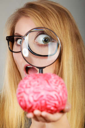 Blonde woman holding magnifying glass investigating something and looking closely at fake brain.