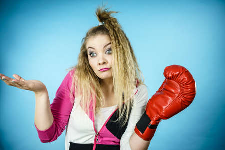 Sporty funny woman wearing red boxing glove gesturing and being confused. Studio shot on blue background.の写真素材