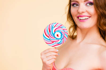 Beautiful woman bare shoulders holding big lollipop candy in hand, closeup. Sweet food and fun concept. Studio shot on brightの写真素材
