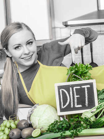Young woman in kitchen having many green vegetables presenting board with diet sign.の写真素材