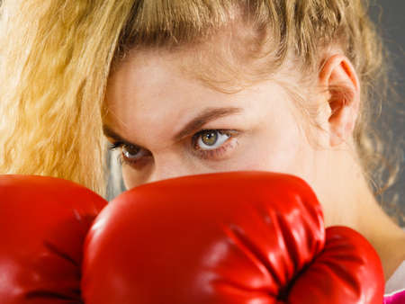 Sporty angry determined woman wearing red boxing gloves, fighting. Studio shot on dark background.
