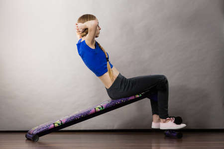Young teenage woman training on bench for sit ups at home. Being fit and healthy, stomach muscles workout.の写真素材