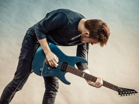 Young bearded man with electric guitar. Adult person is holding instrument and playing. Hobby, music...