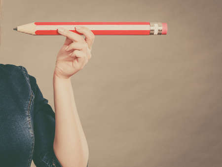 Education, stationery elements, school concept. Female hand student girl or business woman female teacher holding big red pencil. Studio shot on dark grey, toned imageの写真素材