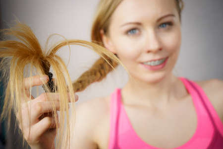 Happy woman looking at her long blonde hair ends, seeing positive effects of using conditioner....