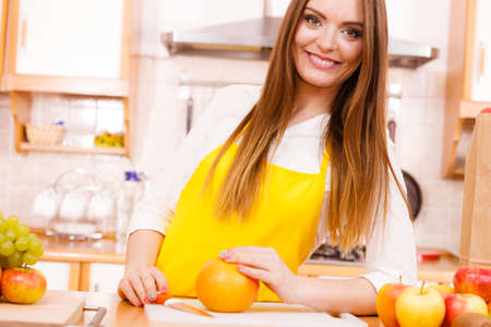 Food cuisine diet fruit natural concept. Smiling lady in kitchen. Female cook leaning on counter next to pile of fruits and kitchenware utensils.の写真素材