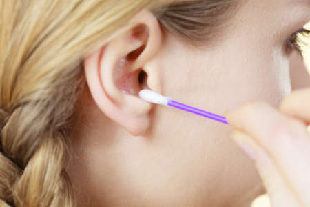 Hygiene concept. Young woman cleaning ear with cotton swabs closeupの写真素材