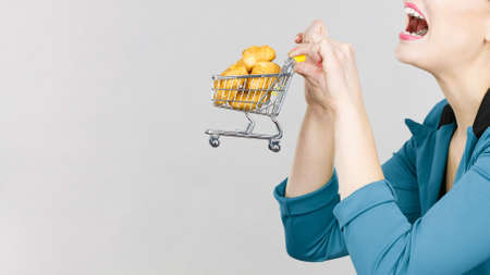 Buying gluten food products concept. Woman hand holding shopping cart trolley with small piece of bread or sweet bunの写真素材