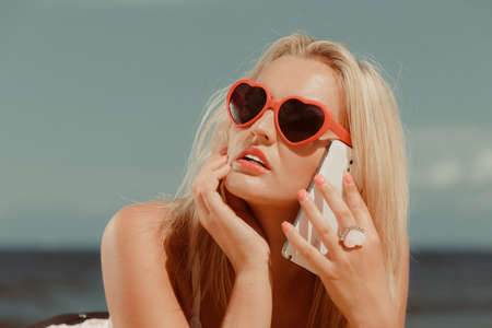 Young girl lying on beach with sunglasses talking using cellular phone. Communication and internet concept.の写真素材