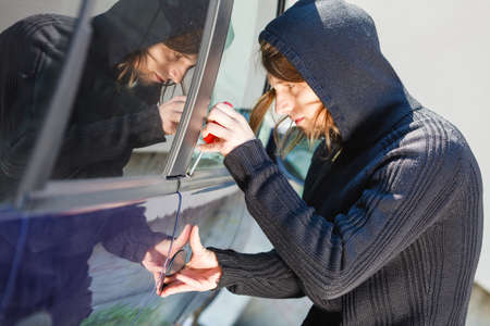 Anti theft system problem concept. Thieft man dressed in black holding screwdriver trying to break...