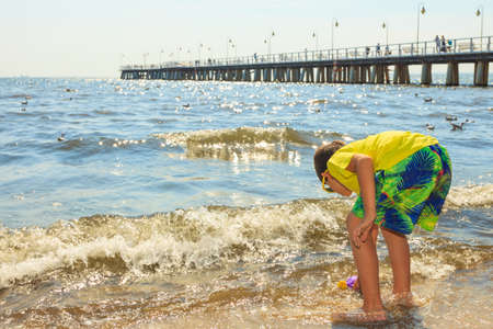 Water fun and joy outside. Little boy walking through the sea ocean. Lonely kid playing outdoors in summer clothes.の写真素材