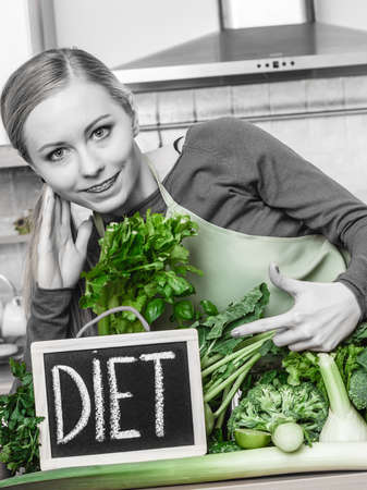 Young woman in kitchen having many green vegetables presenting board with diet sign.の写真素材