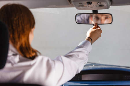 Young man wearing white shirt having long hair, driving car setting mirror inside to see better...