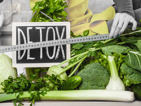 Woman in kitchen having many green vegetables presenting board with detox sign.の写真素材