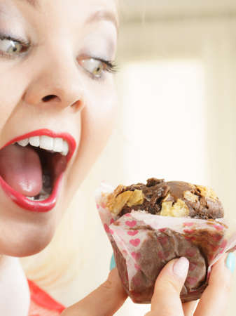 Sweet food sugar make us happy. Attractive blonde woman holds yummy chocolate cupcake in hand, open mouth, craving for cake.の写真素材