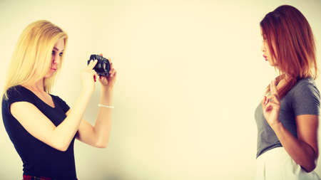 Photographer and model. Blonde girl shooting images, taking photos with camera, photographing mulatto female modelの写真素材
