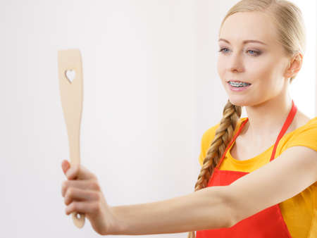 Happy woman holding wooden kitchen spatula with heart love symbol. Cooking utensils concept.の写真素材