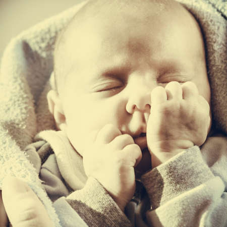 Infant care, beauty of childhood concept. Little newborn baby sleeping calmly in bed surrounded with blankets making funny faces.の写真素材