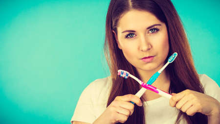 Attractive angry serious woman with long brown hair holding two crossed toothbrushes. Studio shot on blue background.の写真素材