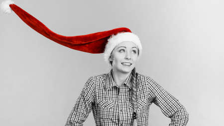 Young woman smiling teen girl wearing blowing santa claus hat. Christmas time. Studio shot on grey,...