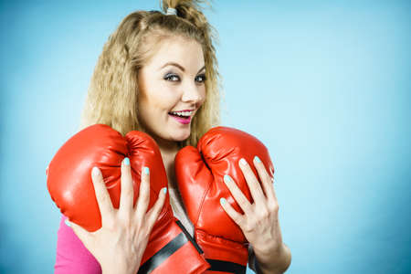 Funny cute blonde girl female boxer with big fun red gloves playing sports boxing studio shot on blueの写真素材