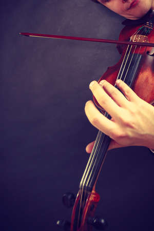 Music passion, hobby concept. Close up young man man dressed elegantly playing on wooden violin. Studio shot on dark backgroundの写真素材