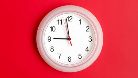 White clock hanging on red wall showing nine hours.の写真素材