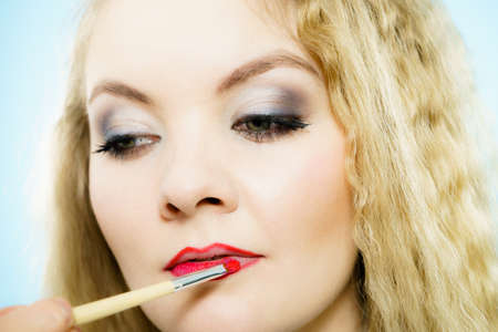 Professional make up artist applying on woman fashion model lips red lip gloss or lipstick using brush. Visage last touch concept.の写真素材