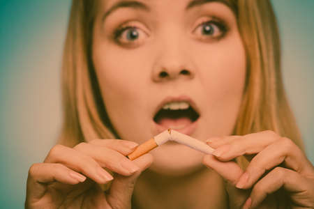 Shocked woman breake down cigarette. Winning with addicted nicotine problems, stop smoking. Quitting from addiction concept. On blueの写真素材