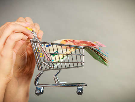 Economy concept. Woman hand holding small shopping cart trolley with money insideの写真素材