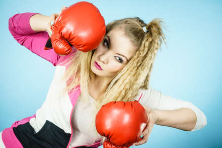 Sporty funny woman wearing red boxing gloves, trying to fight. Studio shot on blue background.の写真素材