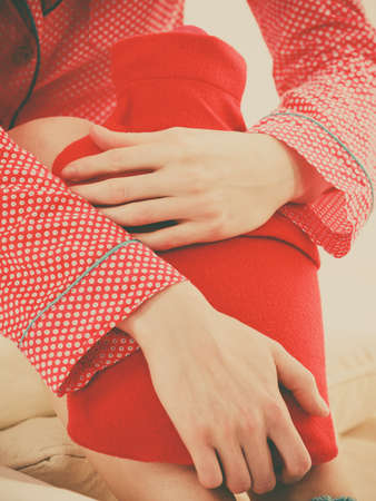 Woman holding warm red hot water bottle, muscle warming up. Fever, flu treatment objects concept.